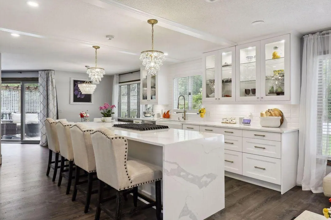 White kitchen with a marble island, cream stools and crystal pendant lights