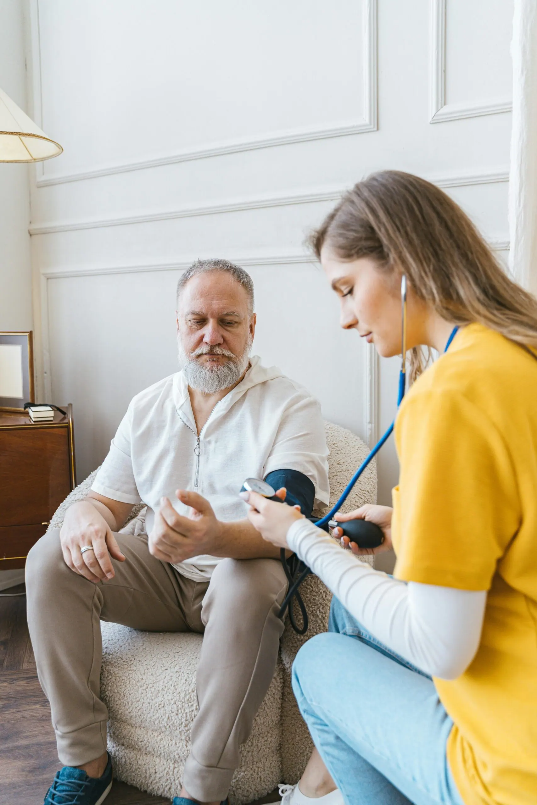 Caregiver checking an older man’s blood pressure in a bright living room (representative photo)
