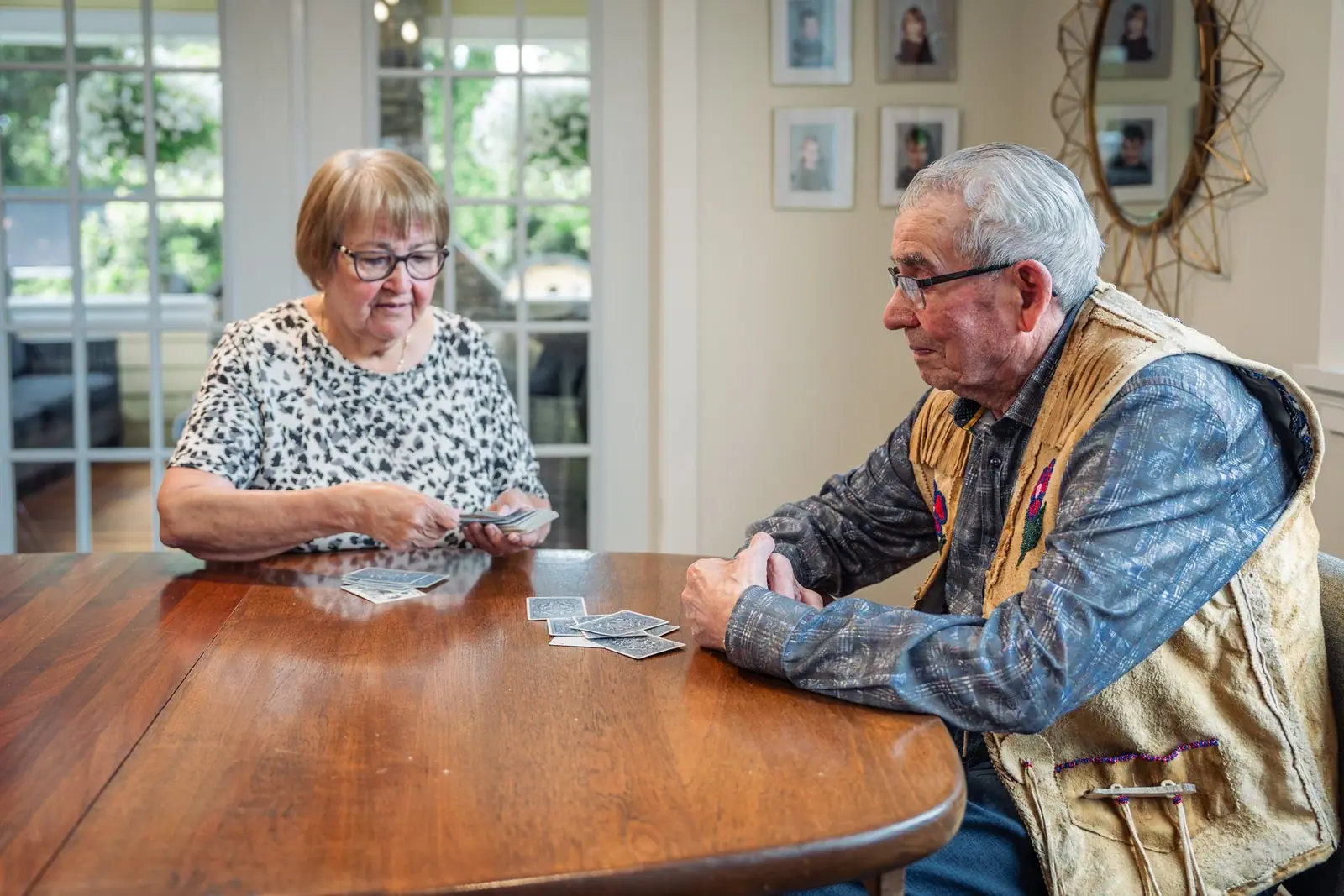 Two older adults playing cards at a round wooden table (representative photo)