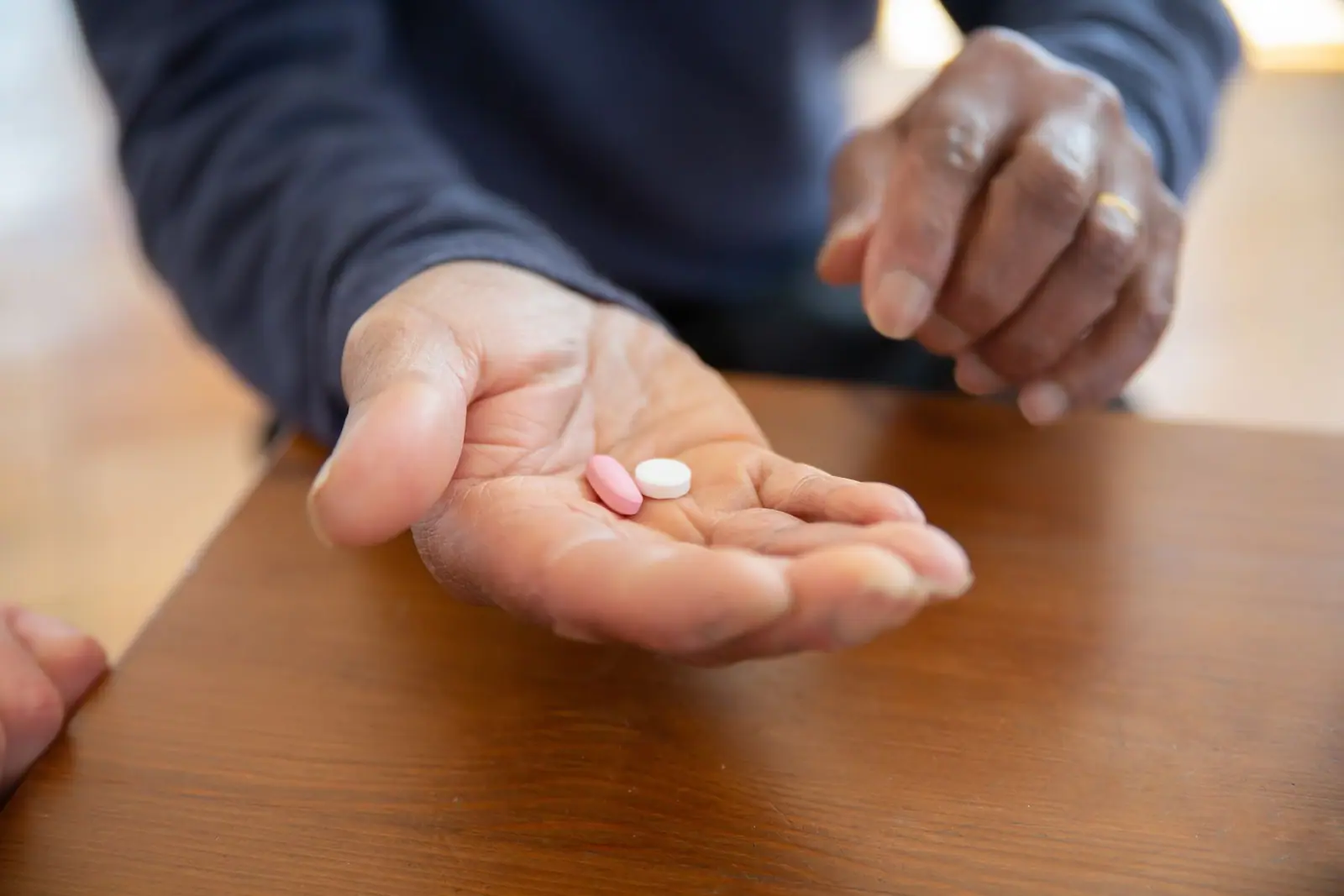 An older person’s open hand holding two tablets over a wooden table (representative photo)