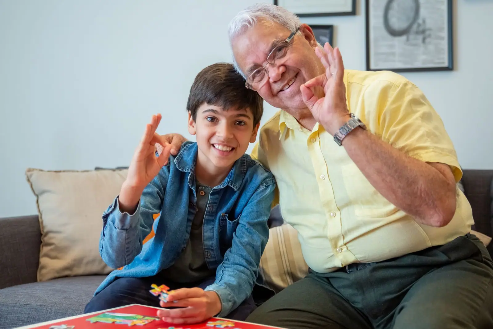 Grandfather and grandson smiling over a jigsaw puzzle on the sofa (representative photo)