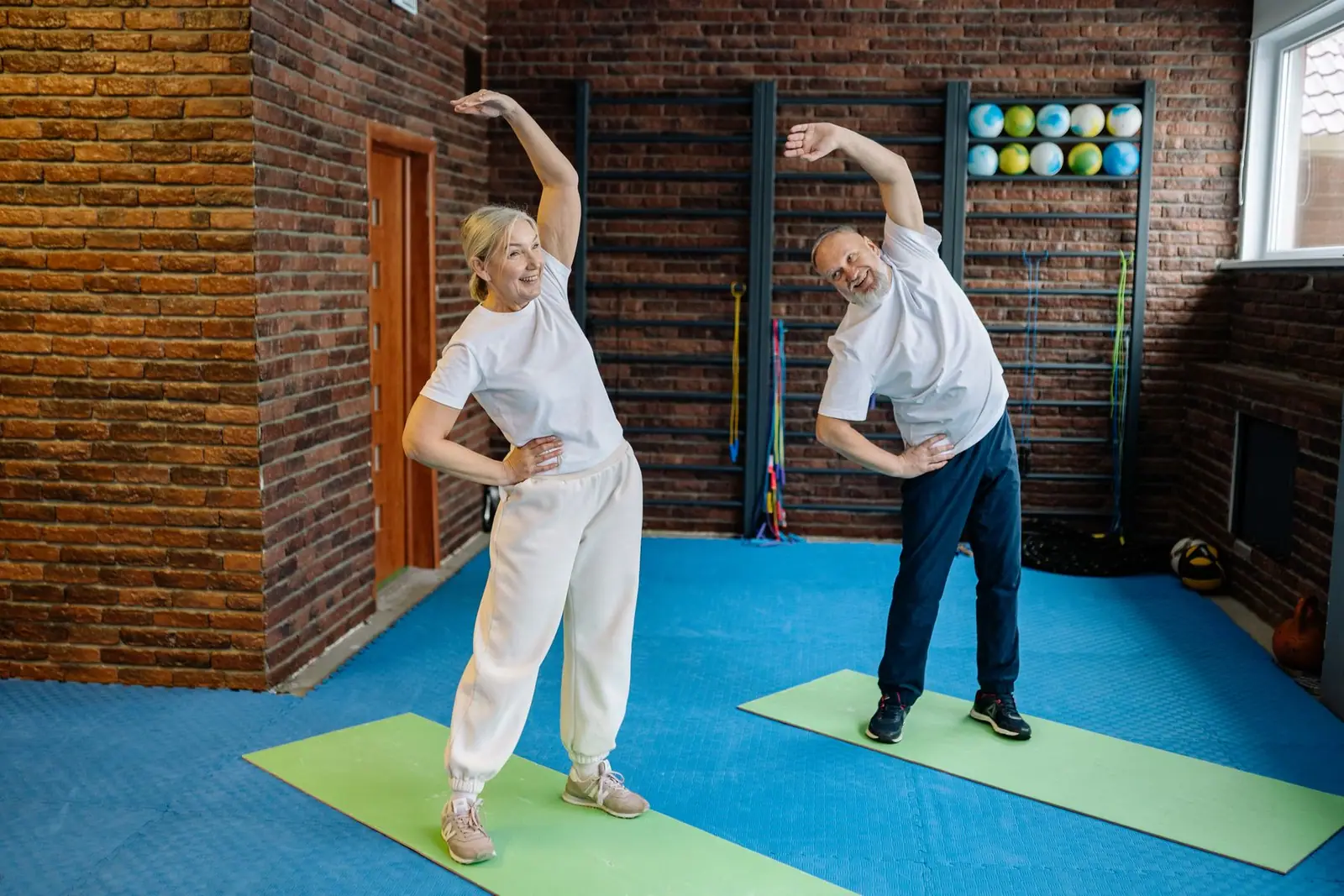 Two older adults doing standing side stretches on exercise mats (representative photo)